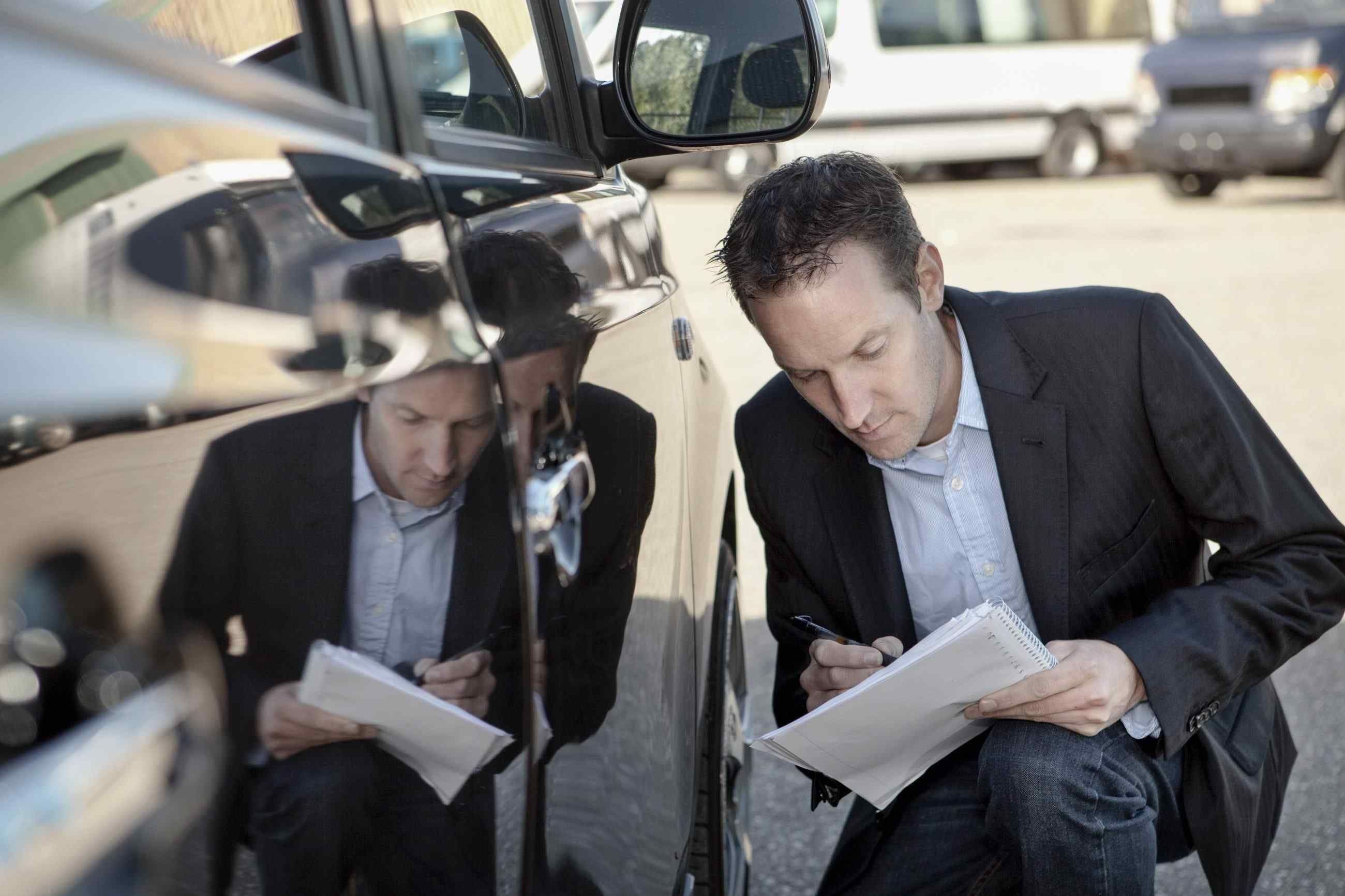 Mann sitter på huk ved en bil og sjekker den grundig ved hjelp av et kontrollskjema