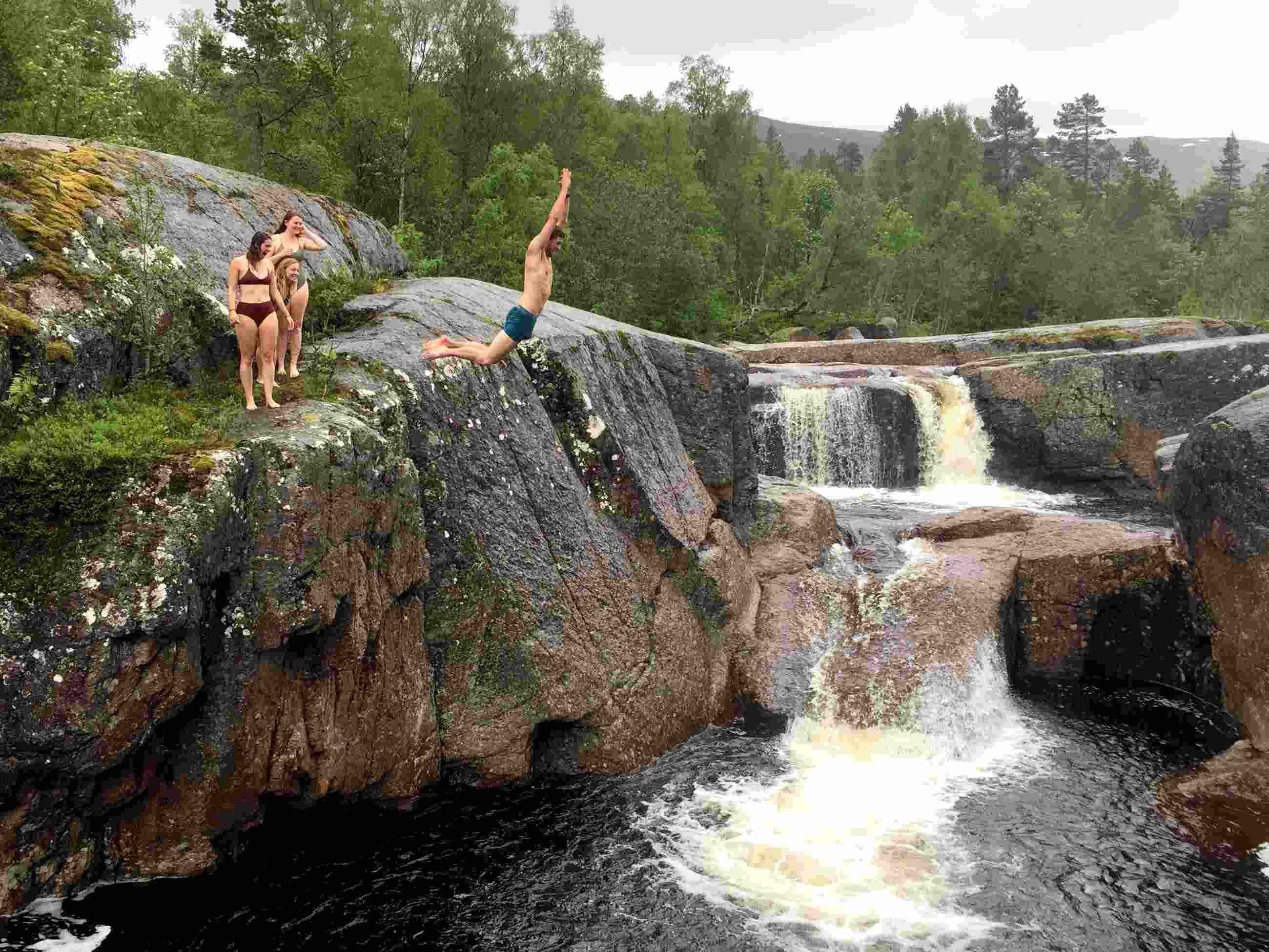 en mann hopper ut i en fossekulp mens vennene ser p&aring;